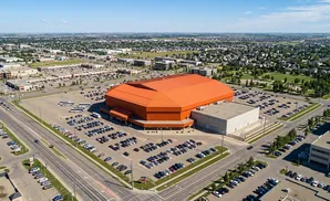Aerial view of an orange domed arena with a large parking lot, surrounded by commercial buildings and residential neighborhoods.