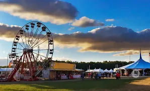 A Ferris wheel and tents at an outdoor fair under a cloudy blue sky.