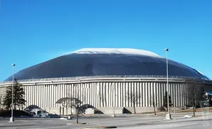 Large domed stadium with a dark roof and a white top, under a clear blue sky.