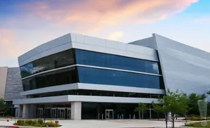 Modern office building with large blue-tinted windows and a silver facade, under a partly cloudy sky.