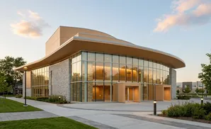 Modern building with stone and glass facade, curved roof, and surrounding landscaped area.