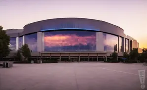 A large modern building with a glass facade reflecting a colorful sunset sky.