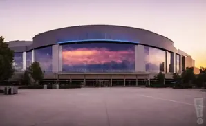Large modern stadium with a reflective glass facade displaying a colorful sunset.
