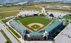 Aerial view of a baseball stadium and surrounding fields on a sunny day.