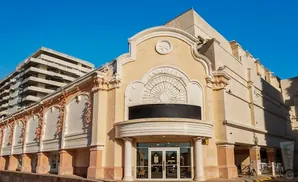 Exterior of a beige building with decorative arches and a sunburst motif, against a bright blue sky.