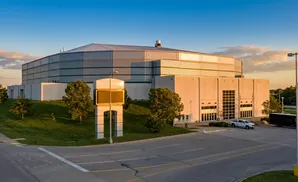 Large arena with a striped facade, an electronic billboard, and parking lot with a truck and van.