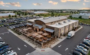 An aerial view of a modern building with an outdoor patio and a parking lot filled with cars.