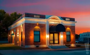 Exterior of a brick building with arched windows and a black awning over the entrance, illuminated at dusk.