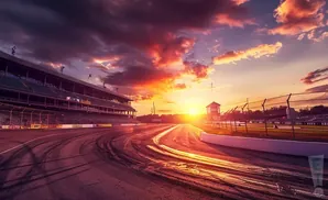 A race track at sunset with dramatic clouds, grandstands, and tire marks.