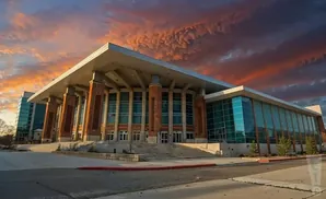 A modern building with brick pillars and glass windows stands under a dramatic sunset sky.