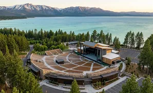 Aerial view of an outdoor amphitheater by a large lake and snow-capped mountains.