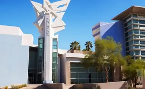 Modern white building with abstract sculpture, blue and glass accents, and palm trees.