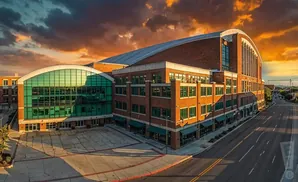 A brick building with a large glass facade, under a dramatic sunset sky.