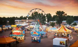 An aerial view of a carnival at sunset with a Ferris wheel, carousel, and food stalls.
