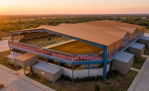 An aerial view of a rodeo arena at sunset, with a tan roof and blue and pink accents.