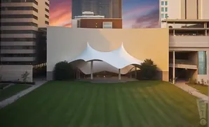 An outdoor amphitheater with a white tent roof and a grassy lawn in front, framed by modern buildings.