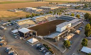 Aerial view of an outdoor rodeo arena with bleachers, a stage, and parking lot.