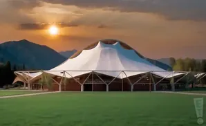 A large tent-like building with a unique, modern design sits in a grassy field at sunset.