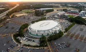 Aerial view of a large oval arena complex with surrounding parking lots and a football stadium.