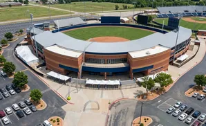 Aerial view of a baseball stadium with a brick building, a baseball field, and surrounding parking lots.