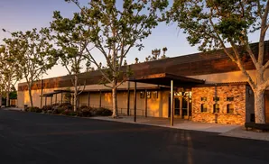 Exterior of a building with large trees and a brick feature, bathed in warm sunset light.