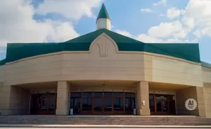 Front view of a beige building with a green, multi-peaked roof and glass doors.