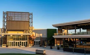 A modern entertainment venue with a large screen, multi-level outdoor seating, and a grassy area.