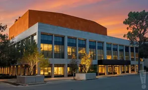 Modern building with large windows and orange brick facade against a colorful sunset sky.