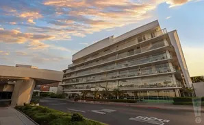 Modern multi-story building with glass balconies at sunset, with a large concrete structure on the left.