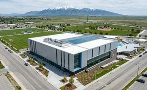 Aerial view of a modern sports complex with soccer fields, a swimming pool, and mountains in the background.
