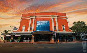 Wide shot of an orange building with a large glass window, under a dramatic sunset sky.