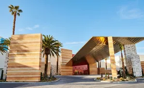 Modern hotel entrance with sandstone walls, a gold roof, and palm trees.