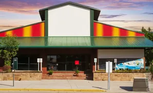 A modern building with a red, yellow, and green facade, featuring large windows and a blank white sign above.