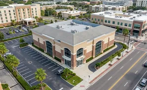 Aerial view of a modern building with a large parking lot, surrounded by other buildings and a street.