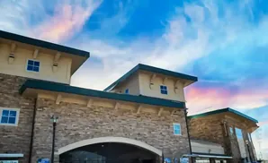 A modern building with stone facade and pitched roofs under a colorful cloudy sky.