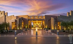 Grand desert hotel entrance at dusk with dramatic sky and warm exterior lighting.
