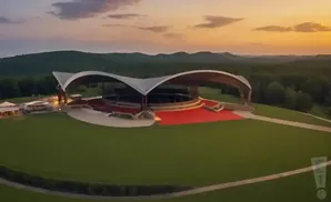 Outdoor amphitheater with a large, curved roof at sunset, surrounded by green hills and trees.