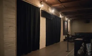 Black velvet curtains cover brick walls in a room with wooden beams, stage lighting, and dark seating.