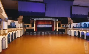 An empty auditorium with a stage, balconies, and a polished floor.