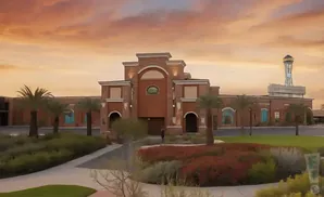 A brick building with arched entrances and palm trees in front under a sunset sky.