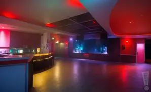 Empty nightclub with a bar and a stage, lit by red and blue lights.