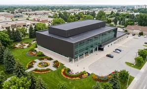 Aerial view of a modern, dark-paneled building with large glass windows, surrounded by lush green lawns and colorful flower beds.