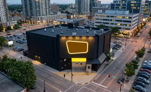 Aerial view of a black building with a glowing orange sign, surrounded by city streets and cars.