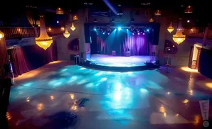 Empty concert venue with a stage, purple curtains, and large ornate chandeliers.