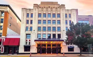 Art deco theater with a lit marquee and blue windows, under a pastel sky.