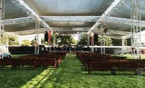 Outdoor concert stage with rows of empty wooden benches on a grassy field.