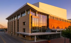 Modern building with beige stone facade and large glass windows reflecting sunset light.