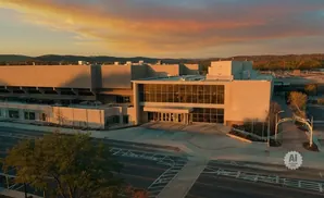 Aerial view of a large, modern building at sunset with golden light on its facade and a colorful sky.