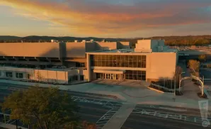 Aerial view of a large, modern convention center at sunset, with warm light illuminating its facade.