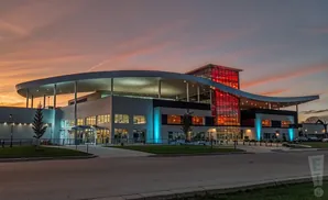 Modern building with a curved roof and red glass tower at sunset.